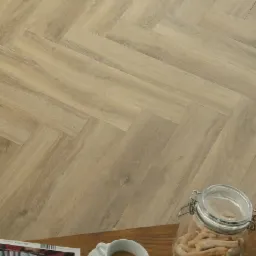 Jasne panele ułożone we wzór jodełki francuskiej, na pierwszym planie kawa, gazeta i słoik z paluszkami.