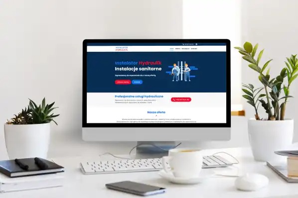 Ekran komputera prezentuje stronę internetową instalatora hydrauliki sanitarnej na biurku z roślinami, kawą i akcesoriami biurowymi.