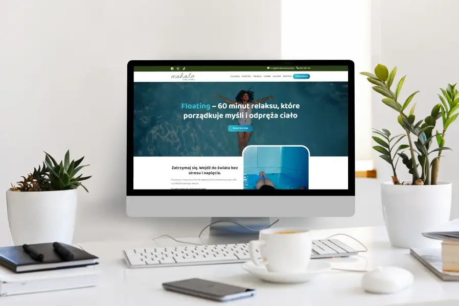 Ekran komputera iMac prezentujący stronę internetową Floating Tychy na minimalistycznym biurku z roślinami, kawą i akcesoriami biurowymi.