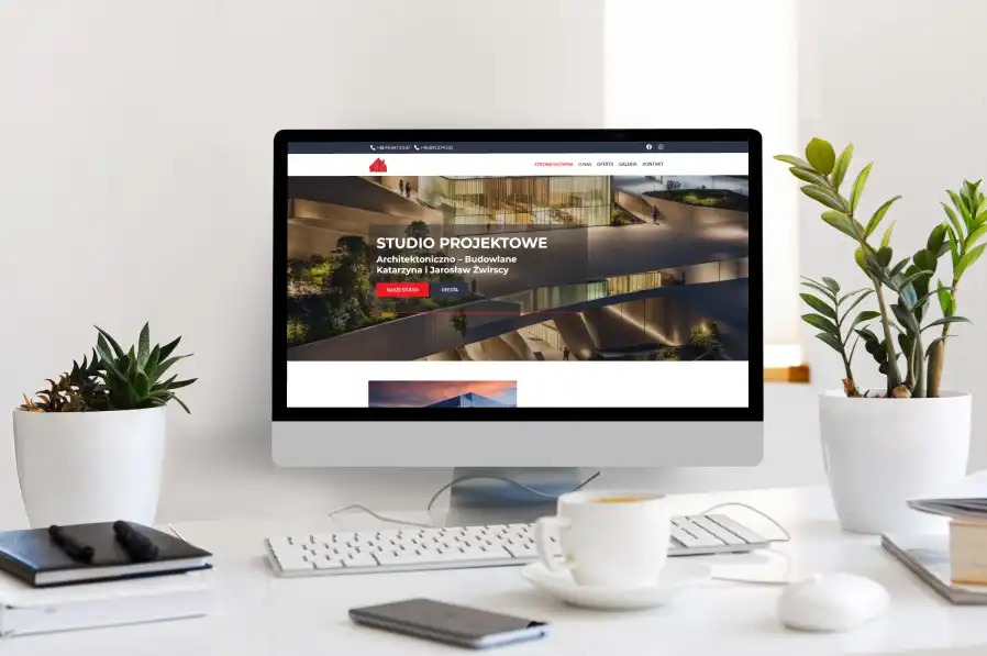 Ekran komputera prezentujący stronę internetową architektonicznego studia projektowego na tle minimalistycznego biurka z roślinami i kawą.