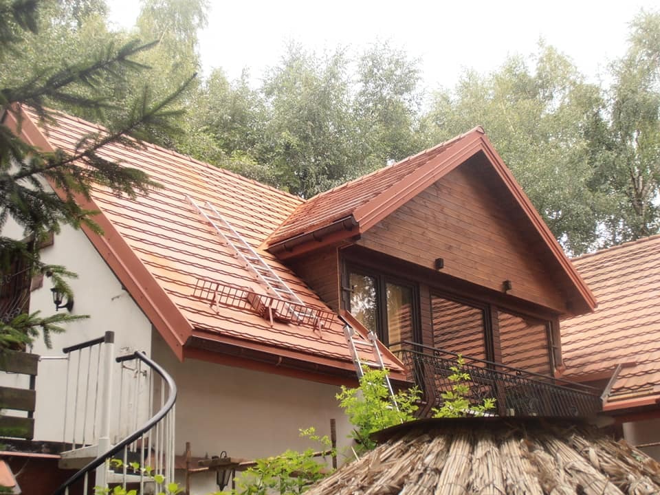 Dom z nową, czerwoną dachówką, drewnianą nadbudówką i spiralnymi schodami, z drabiny na dachu