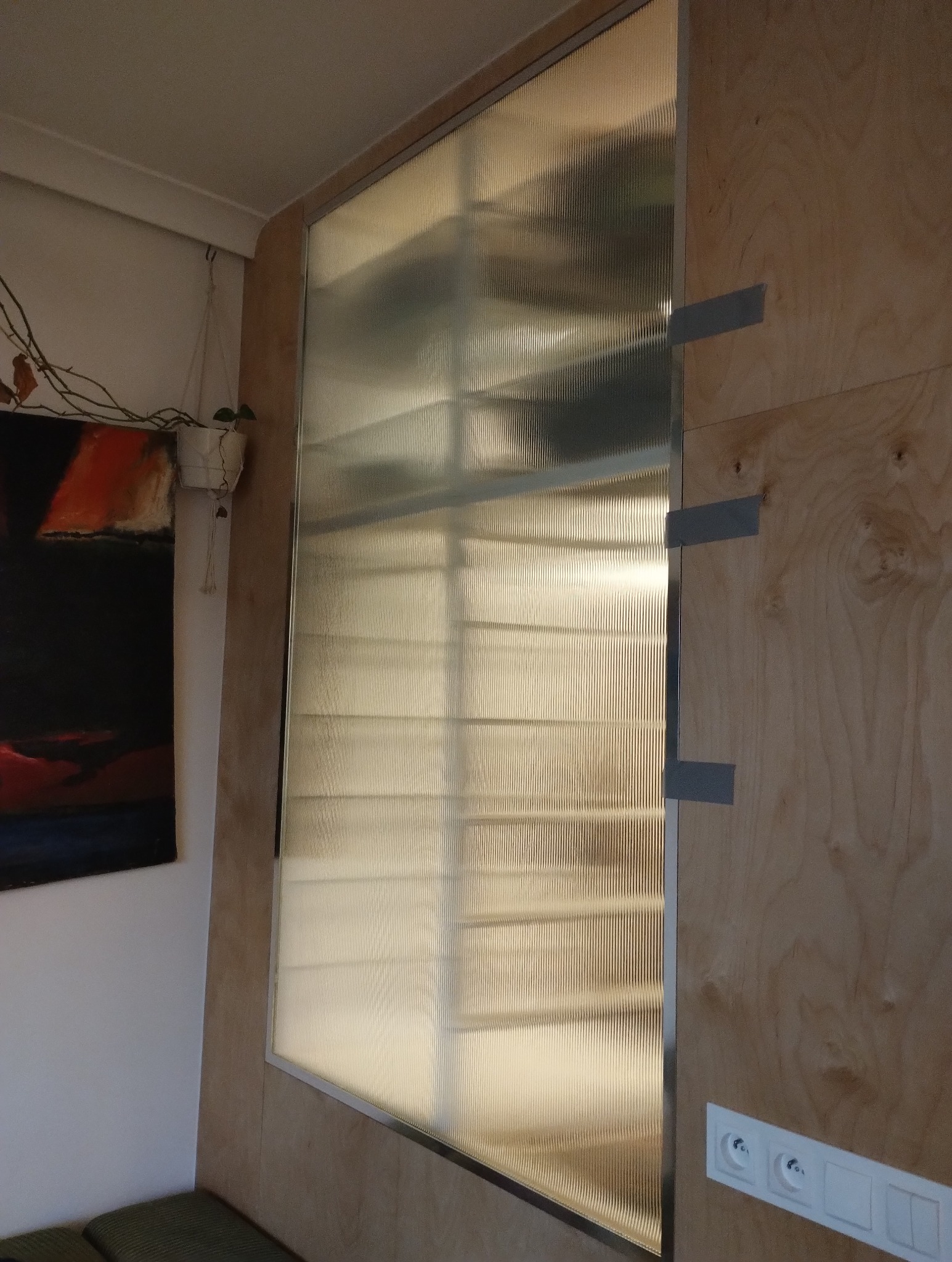 Wstawiona szyba ryflowana w drewnianej ramie, zabezpieczona taśmą montażową, widok z bliska na strukturę szkła i detale wykończenia.