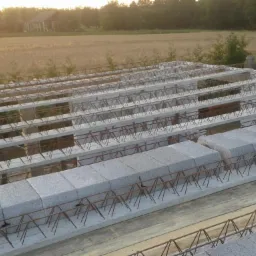 Konstrukcja stropu Teriva z betonowymi belkami i pustakami, widok z góry na tle krajobrazu wiejskiego w słoneczny dzień. Etap budowy domu.