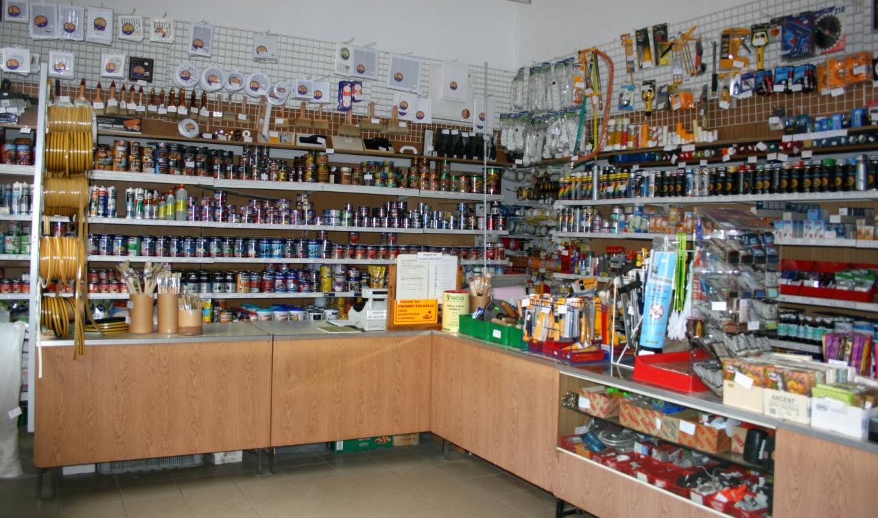 Wnętrze sklepu budowlanego: pełne półki z farbami, lakierami, pędzlami i innymi akcesoriami malarskimi, widok zza lady.