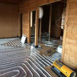 Układanie rur ogrzewania podłogowego w drewnianym domu, widoczny rozdzielacz i narzędzia. Rury ułożone na siatce, przygotowane do zalania wylewką.