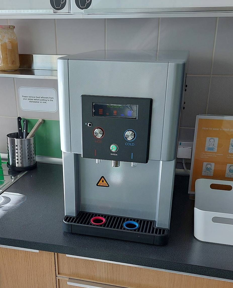 Dystrybutor wody z opcjami gorącej, zimnej i gazowanej wody, marki Ruhens, umieszczony na blacie w pomieszczeniu biurowym.