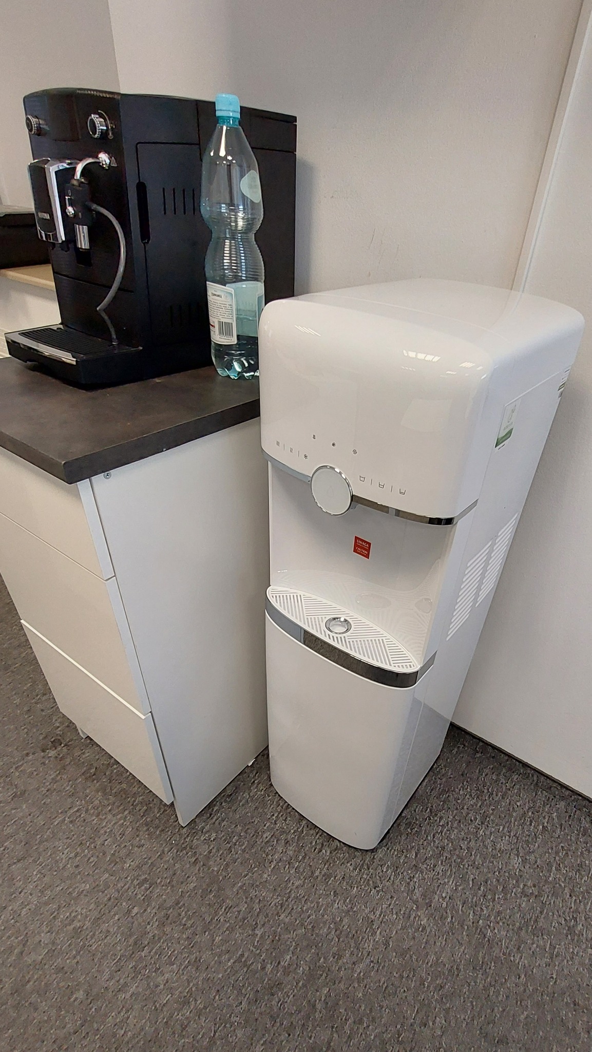 Ekspres do kawy i dystrybutor wody stoją obok siebie w Siemiatyczach, na blacie stoi butelka wody.