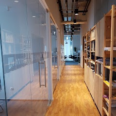 Wnętrze nowoczesnego biura z przeszklonymi ścianami i drewnianą podłogą, widok na korytarz z regałami po prawej stronie.