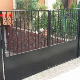 Czarna, metalowa brama z ozdobnymi elementami, widok z zewnątrz po montażu. Brama prowadzi do zejścia do piwnicy.