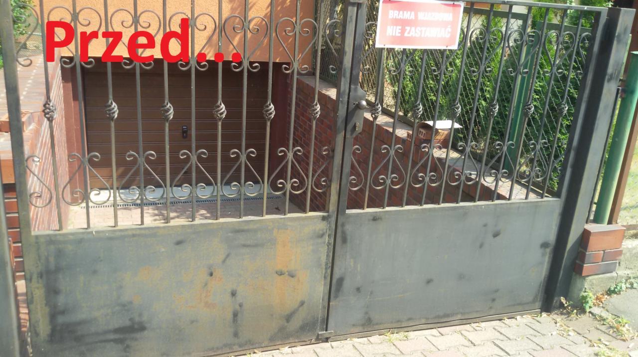 Zardzewiała, metalowa brama wjazdowa z dekoracyjnymi elementami, widoczna z bliska. Na bramie napis 'Przed...'. W tle brama garażowa i tabliczka informacyjna.
