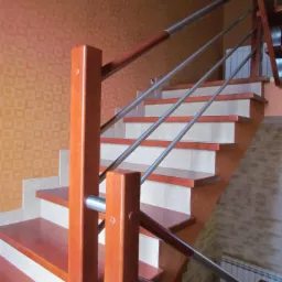 Drewniane schody z metalową balustradą w pomarańczowym wnętrzu. Widoczne detale wykończenia i połączenia materiałów. Ujęcie od dołu, ukazujące konstrukcję schodów.