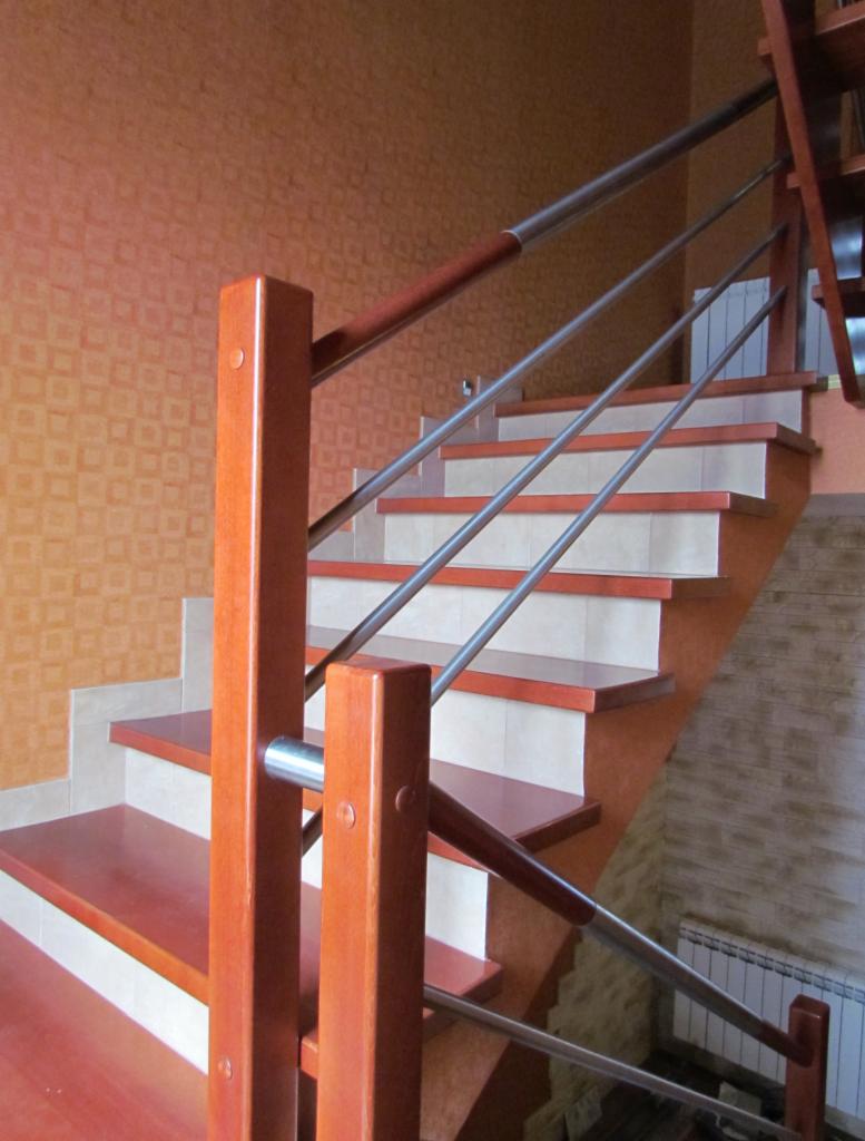 Drewniane schody z metalową balustradą w pomarańczowym wnętrzu. Widoczne detale wykończenia i połączenia materiałów. Ujęcie od dołu, ukazujące konstrukcję schodów.