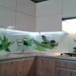 Nowoczesna kuchnia z drewnopodobnymi szafkami i szklanym panelem ściennym z motywem aloesu, podświetlonym listwą LED.