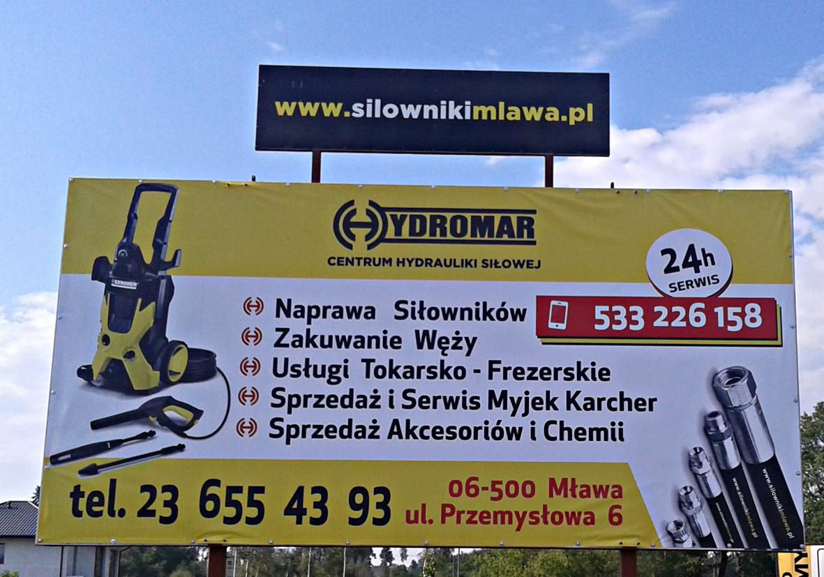 Billboard reklamowy firmy Hydromar z Mławy, oferującej naprawę siłowników, zakuwanie węży, usługi tokarsko-frezerskie oraz sprzedaż i serwis myjek Karcher; widoczny numer telefonu i adres strony...