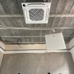 SM SYSTEM - Kasetonowa jednostka klimatyzacji marki Totenso zamontowana w surowym wnętrzu z widocznymi elementami instalacji i drabina, sugerująca etap montażu.