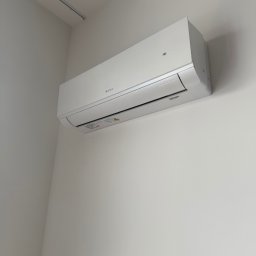 SM SYSTEM - Biały klimatyzator marki Gree zamontowany na jasnej ścianie. Widoczny z bliska, z delikatnym oświetleniem. Minimalistyczny design.