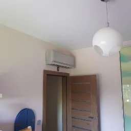 Zamontowany klimatyzator w pokoju dziecięcym w Łodzi, widoczny dyplom na półce i lampa sufitowa w kształcie kuli.