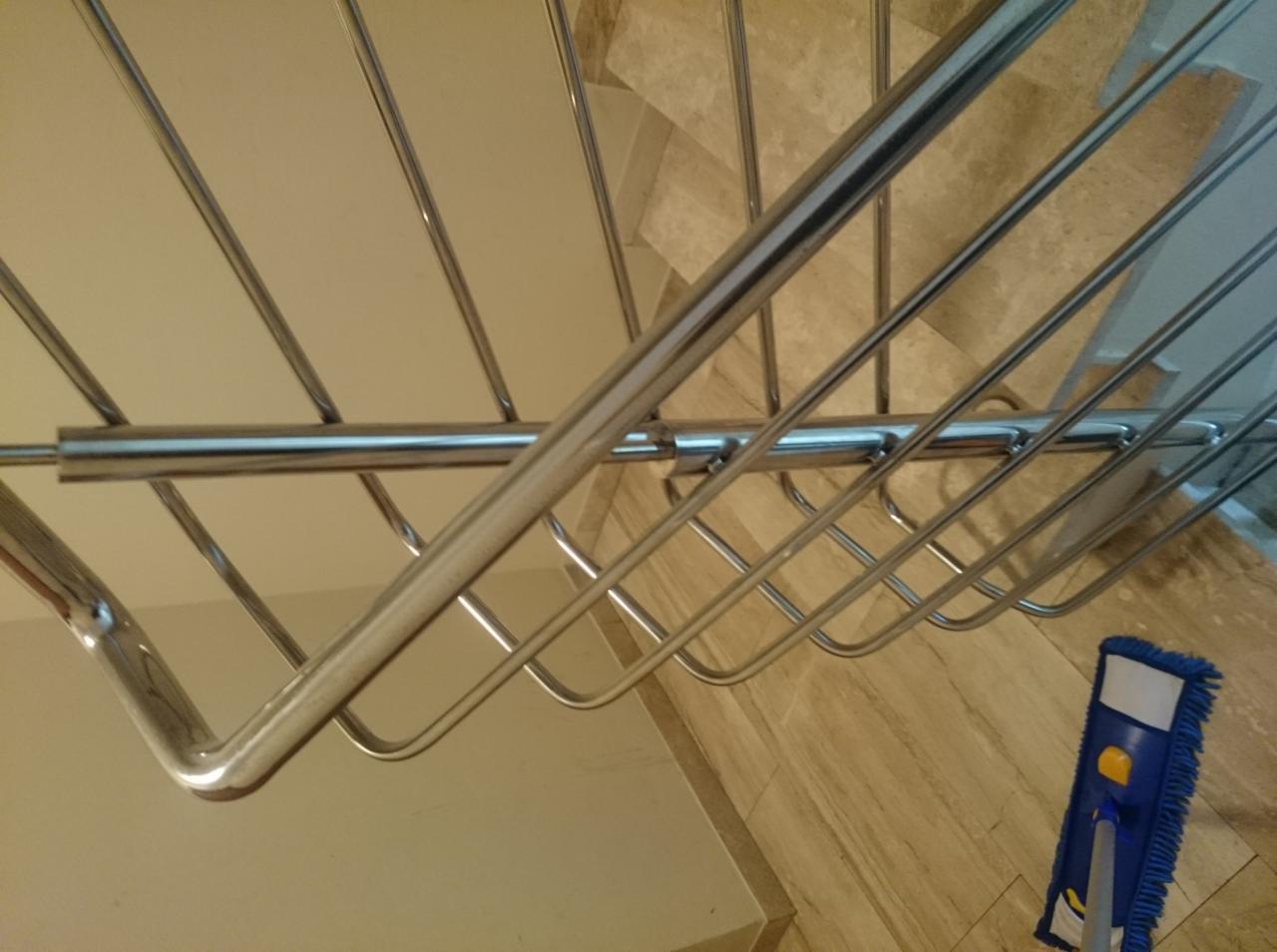 Mop parowy z niebieską nakładką z mikrofibry, oparty o marmurowe schody, widziany z góry spod chromowanej barierki schodowej, podczas sprzątania wnętrza.