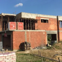Budowa domu jednorodzinnego w Wyry w trakcie wznoszenia murów z czerwonej cegły Porotherm, widoczne rusztowania i materiały budowlane na placu budowy.