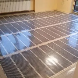 Rozłożone maty grzewcze na podłodze w pokoju, przygotowane do zalania wylewką. Widoczny grzejnik na ścianie i okno balkonowe. SH Korea.