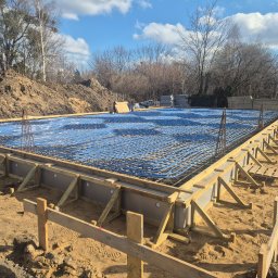 H&R PROJEKT SP. ZO.O. - Fundament z ułożonymi rurami ogrzewania podłogowego i zbrojeniem, przygotowany do zalania betonem. Widoczne drewniane szalunki i ziemne otoczenie.