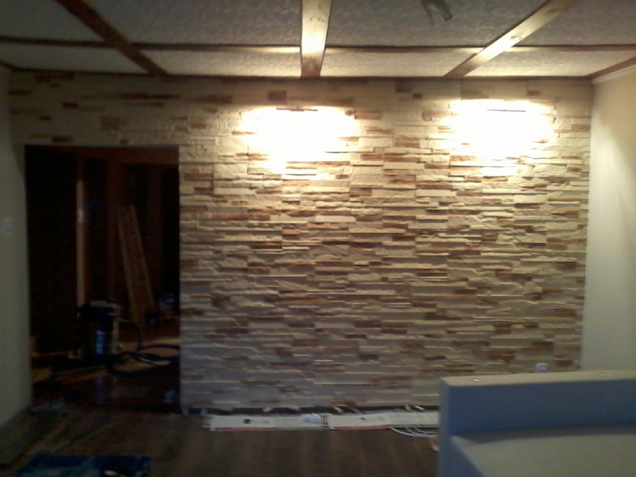 Ściana z dekoracyjnej cegły podświetlona lampami, drewniany sufit i otwarte przejście. Wykończenie wnętrza z elementami dekoracyjnymi.