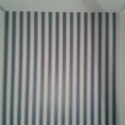 Fragment ściany z pionowymi, szaro-białymi pasami, wykończonej listwą przypodłogową.