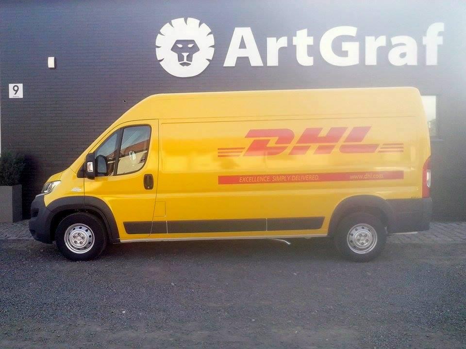 Żółty samochód dostawczy DHL zaparkowany na tle ciemnej ściany budynku z logo ArtGraf i numerem 9, widok z boku, oświetlenie dzienne.