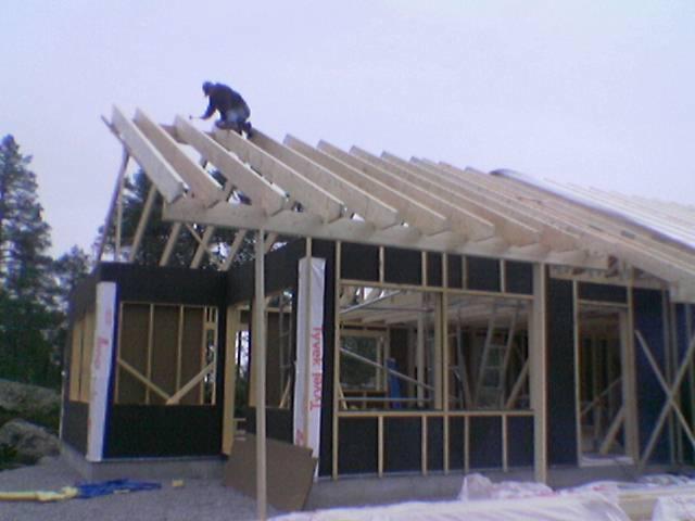 Budowa domu w konstrukcji szkieletowej: monter na dachu mocuje krokwie. Widoczne ściany z płyt OSB i folia izolacyjna.