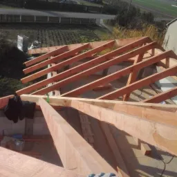 Konstrukcja drewniana dachu w trakcie budowy w Borkach, widoczne krokwie i więźba dachowa, bloczki betonowe oraz materiały budowlane w tle.