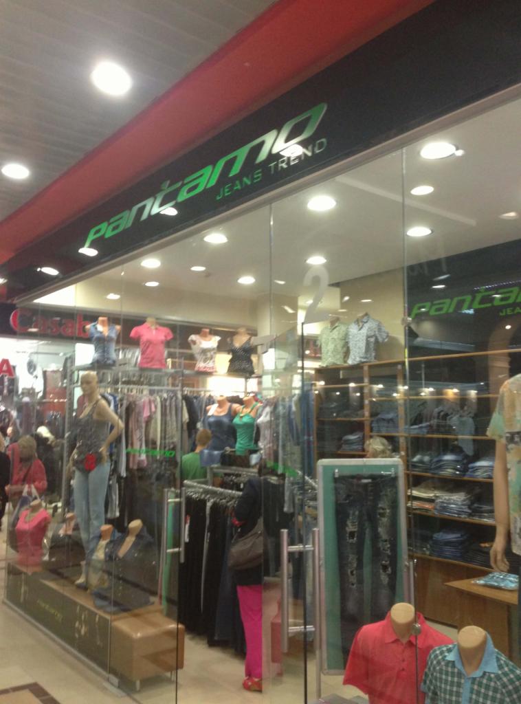 Wnętrze sklepu odzieżowego Pantamo Jeans Trend z manekinami i ubraniami wewnątrz, widoczne przez szklaną witrynę. Jasne oświetlenie, różnorodność asortymentu.