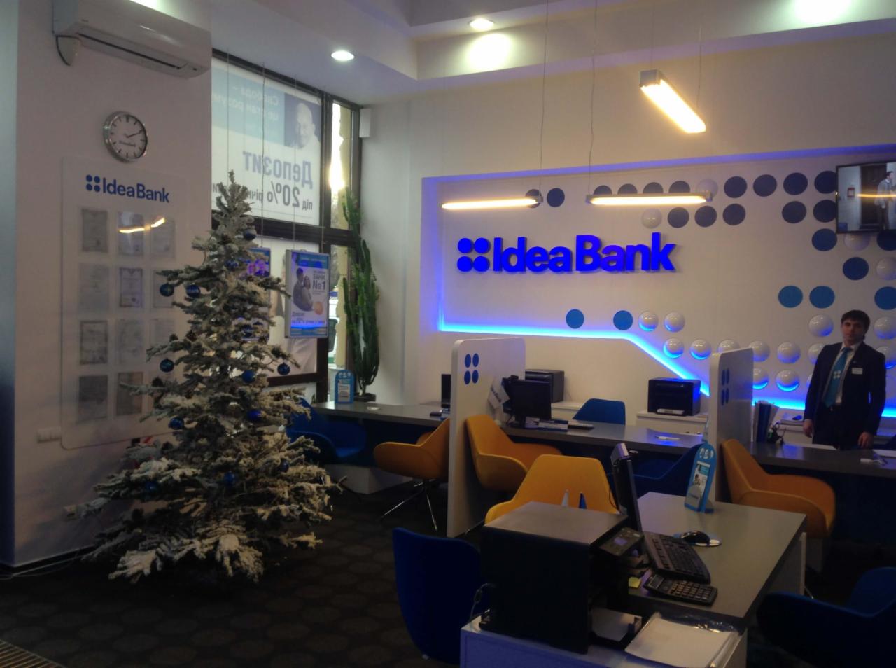 Wnętrze placówki Idea Bank w Warszawie, z podświetlonym logo, stanowiskami obsługi klienta i choinką. Widoczny pracownik w tle.