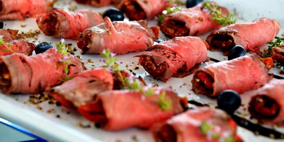 Roladki z rostbefu wypełnione suszonymi pomidorami i bazylią, udekorowane jagodami i ziołami na białym talerzu.