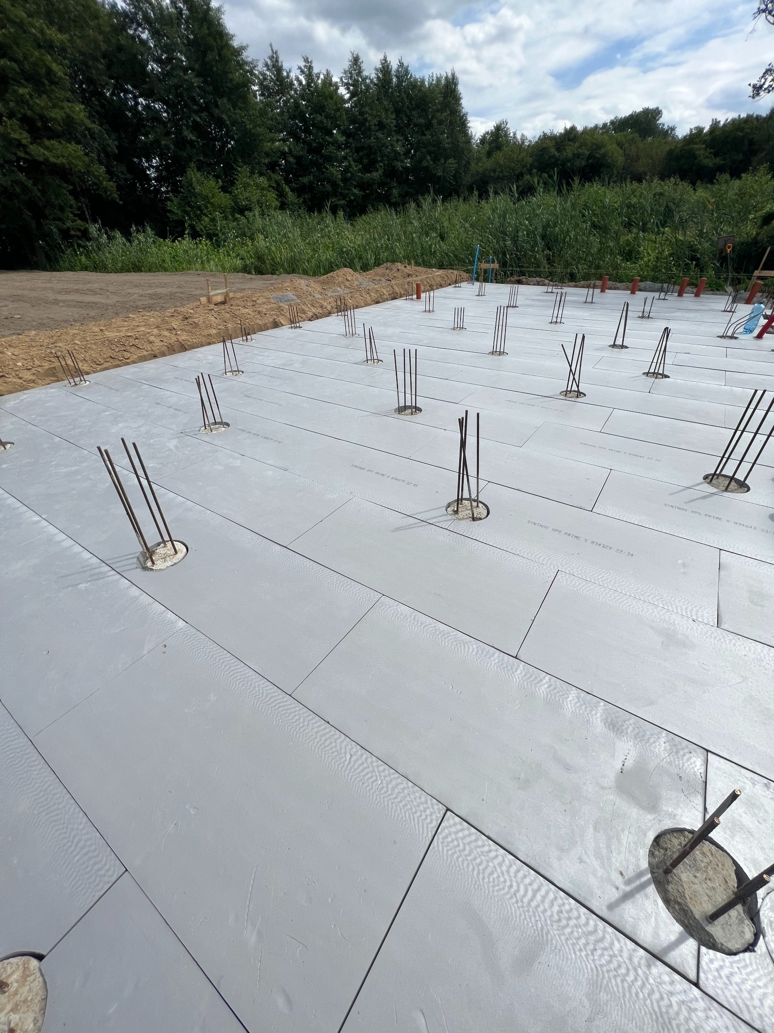 Przygotowany teren pod budowę domu z ułożonymi płytami izolacyjnymi i wystającymi prętami zbrojeniowymi, widok z góry.