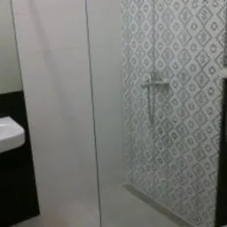 Mała łazienka po remoncie: biała umywalka na czarnym blacie, kabina prysznicowa z geometrycznymi płytkami w odcieniach szarości, widok z niskiego kąta.