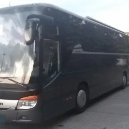 Czarny autokar Setra zaparkowany na betonowym placu przed budynkiem z rzędami okien.