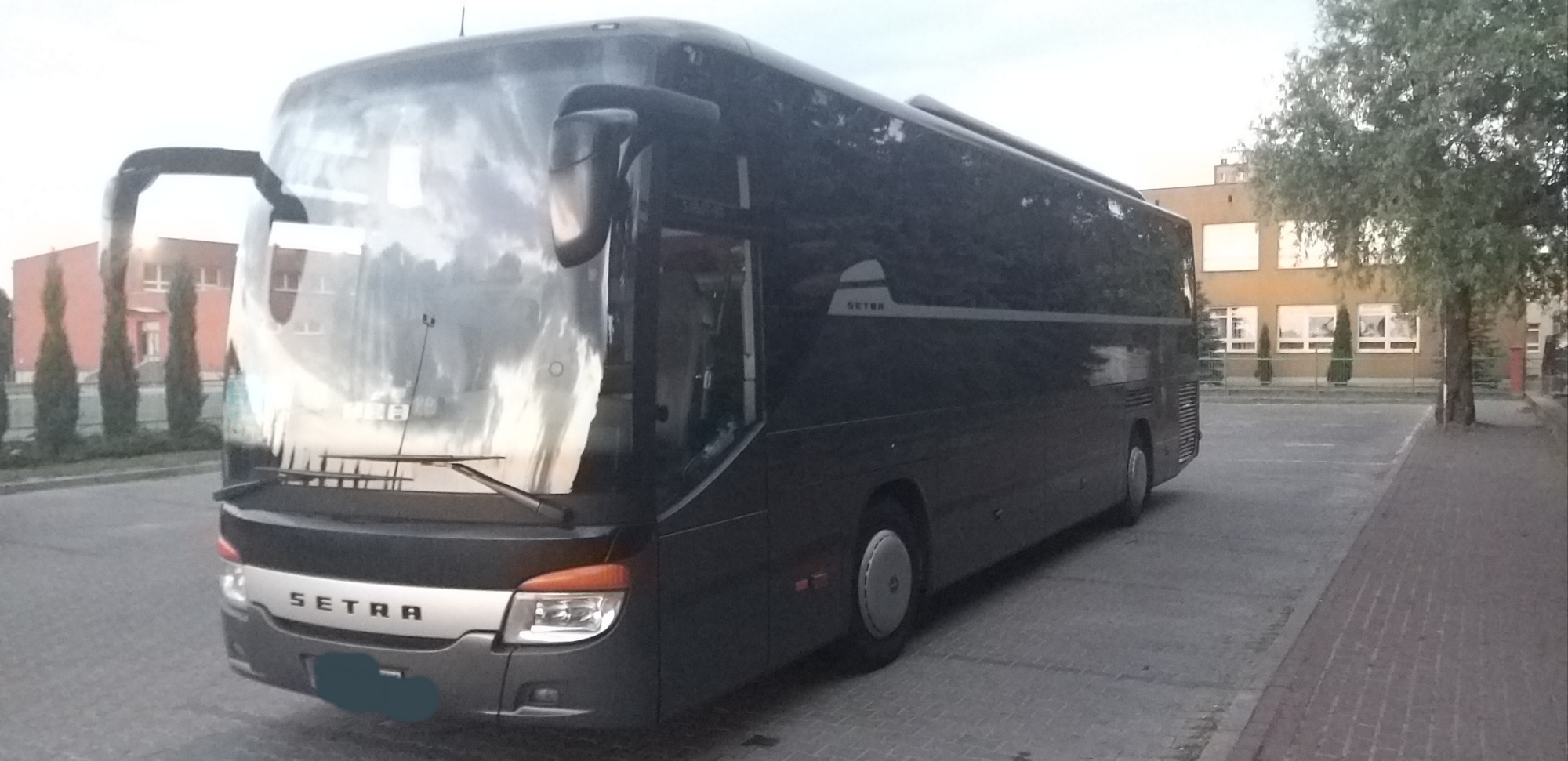 Czarny autokar Setra zaparkowany na betonowym placu przed budynkiem z rzędami okien.