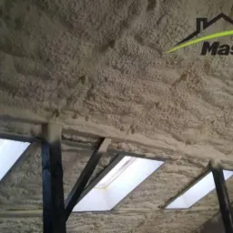 Poddasze z oknami dachowymi pokryte grubą warstwą izolacji natryskowej, widoczne fragmenty konstrukcji drewnianej i logo firmy MasterPUR.