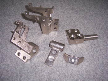 Metalowe elementy po obróbce, różne kształty i rozmiary, widoczne ślady obróbki skrawaniem, nierówna powierzchnia tła.