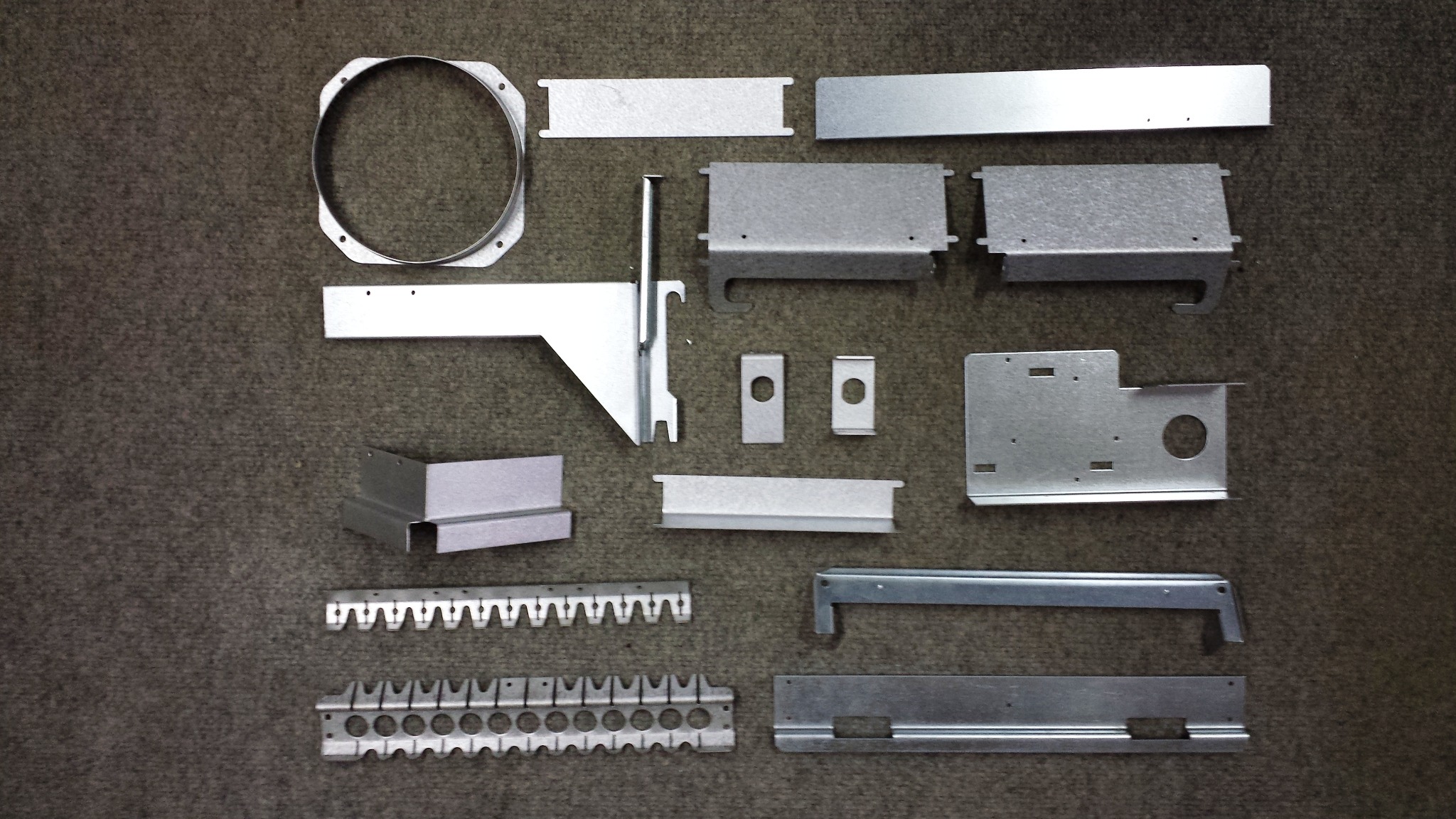 Precyzyjnie wykonane, metalowe komponenty o różnych kształtach i rozmiarach, wyprodukowane w Świebodzicach, ułożone na szorstkim, ciemnym tle.