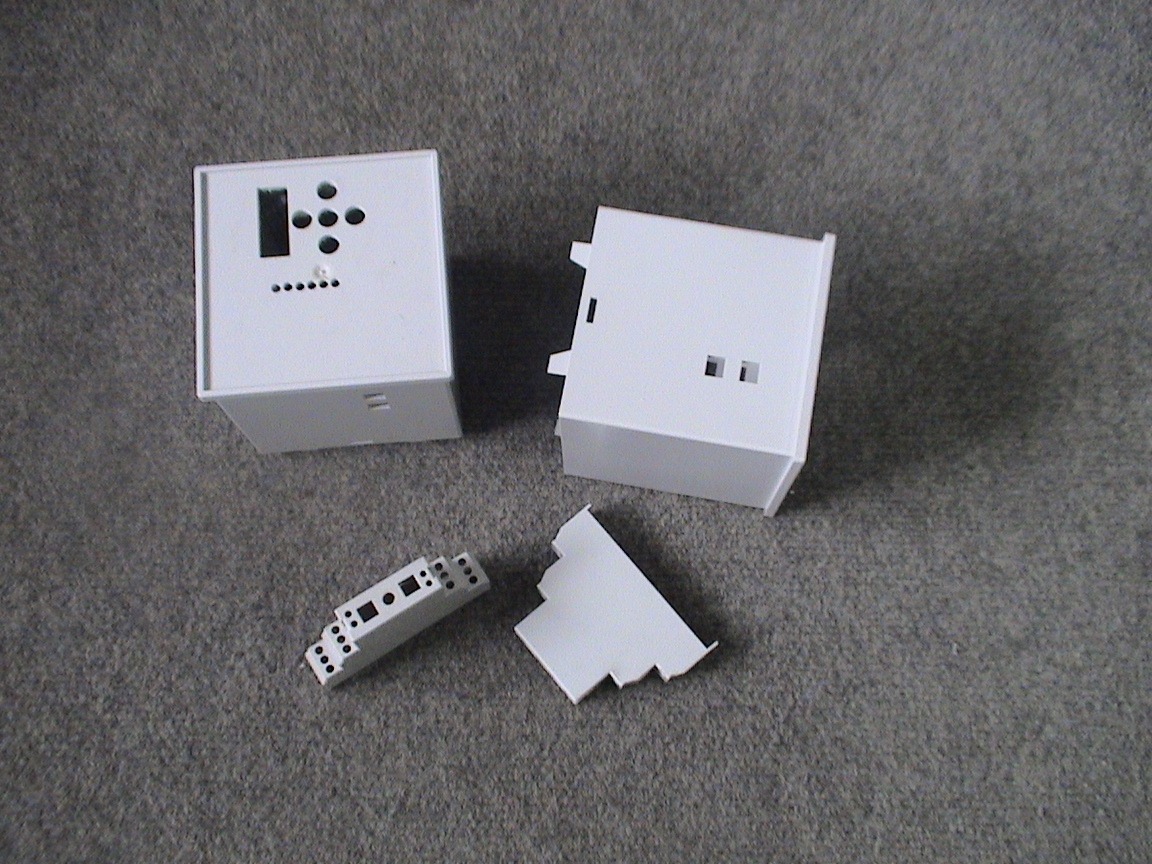 Białe obudowy elektroniczne z otworami, wykonane z tworzywa, leżą na szarym tle. Jeden z elementów jest rozmontowany.