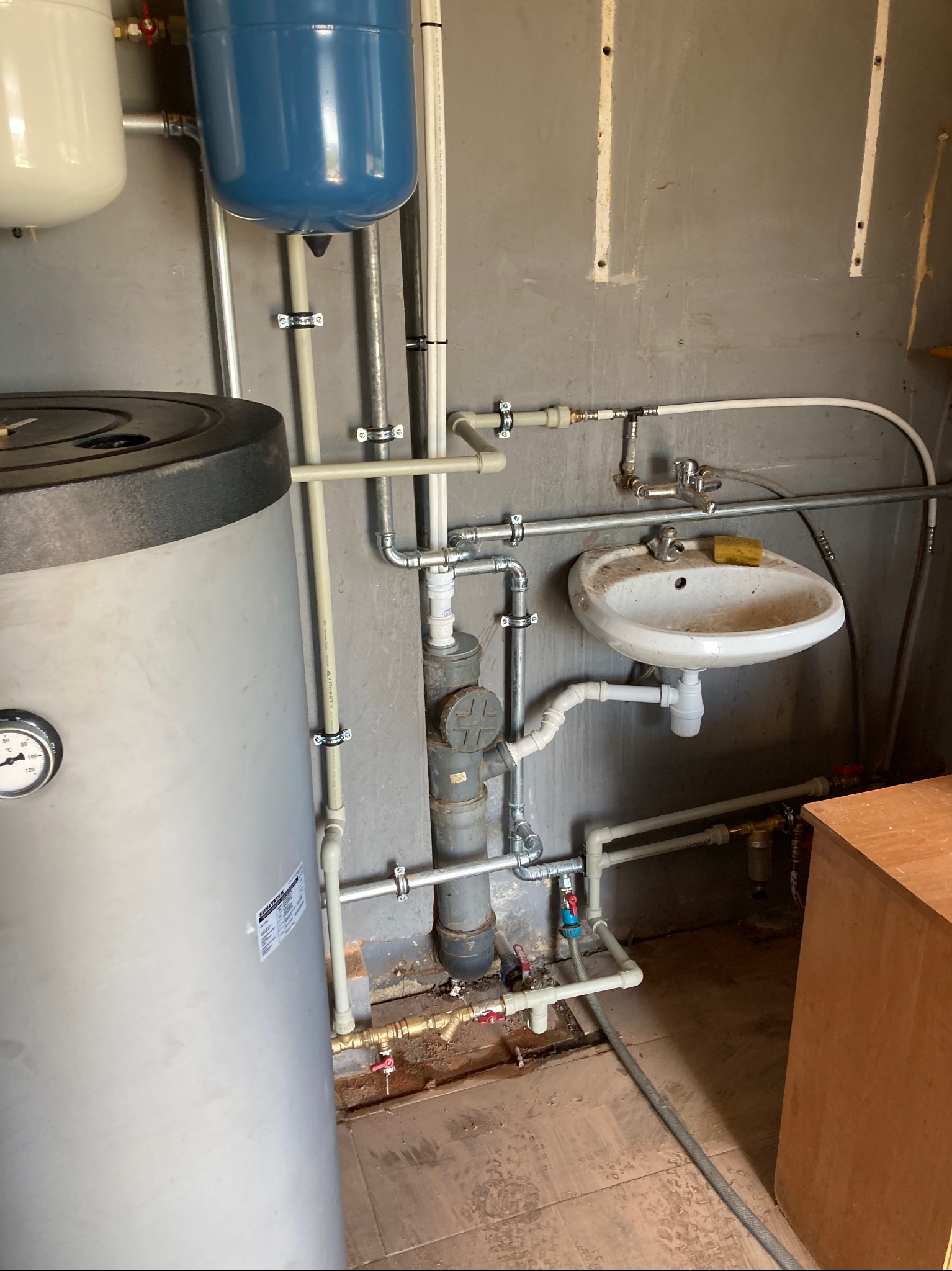 Instalacja wodna z dwoma zbiornikami ciśnieniowymi, bojlerem i umywalką w pomieszczeniu z surowymi ścianami.