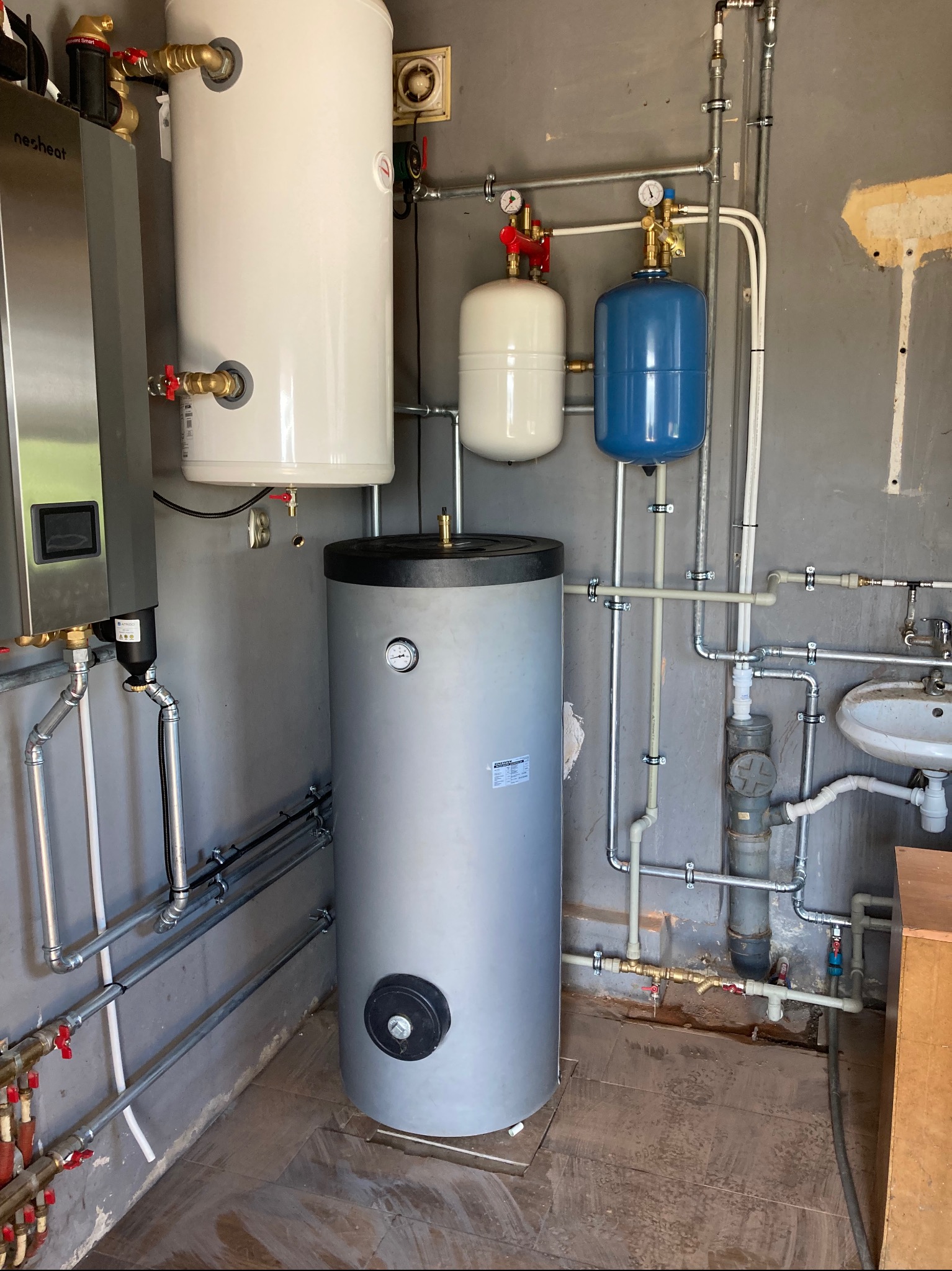 Złożona instalacja grzewcza i hydrauliczna w kotłowni w Radomiu, zawierająca zasobnik ciepłej wody, zbiorniki wyrównawcze oraz piec gazowy marki Nesheat.