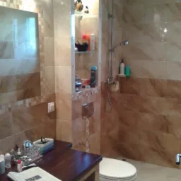 Wykończona łazienka z beżowymi płytkami i wnęką z półkami w Zawoni. Widoczna umywalka z blatem, toaleta i kabina prysznicowa z deszczownicą.