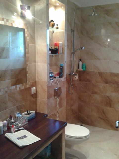 Wykończona łazienka z beżowymi płytkami i wnęką z półkami w Zawoni. Widoczna umywalka z blatem, toaleta i kabina prysznicowa z deszczownicą.