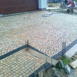 DJD-bruk - Ułożona kostka granitowa w kształcie wachlarza przed garażem. Widoczne obrzeża z ciemnej kostki i elementy przygotowane do dalszych prac.