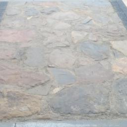 DJD-bruk - Nieregularna kamienna nawierzchnia obramowana kostką brukową w odcieniach szarości i bieli, tworząca kontrastowy wzór. Widok z góry, neutralne oświetlenie.