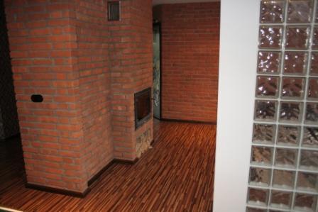 Wnętrze z ceglaną ścianą i kominkiem, parkietem oraz ścianą z luksferów. Widoczne detale wykończenia i aranżacji wnętrza.