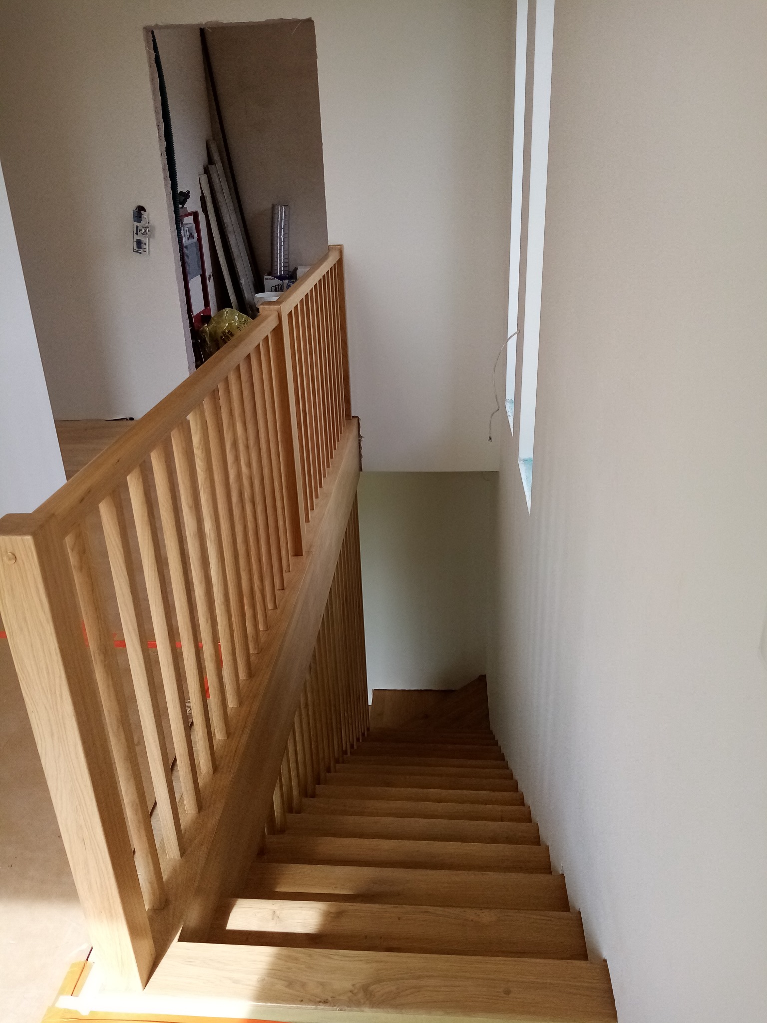 Jasne drewniane schody z balustradą w nowym domu, widok z góry. Elementy wykończeniowe w tle, surowe ściany i okno bez parapetu.