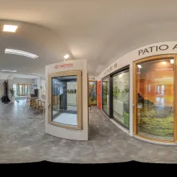 Wnętrze salonu z ekspozycją różnych modeli okien i drzwi przesuwnych, w tym okna z widokiem na krajobraz, oraz drzwi z czarną ramą i szybą.